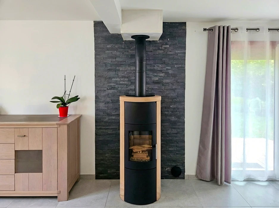 Intérieur moderne avec poêle à bois cylindrique noir et habillage bois clair, posé devant un parement mural en ardoise noire